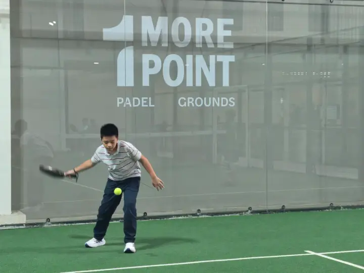 Player hitting a forehand in front of the 1More Point glass